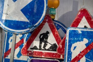 Mixture of construction signs including colours of clue red and white. Centre image is silhouette of a man digging dirt